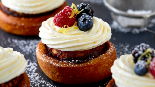 Cinnamon roll topped with whipped cream and berries.